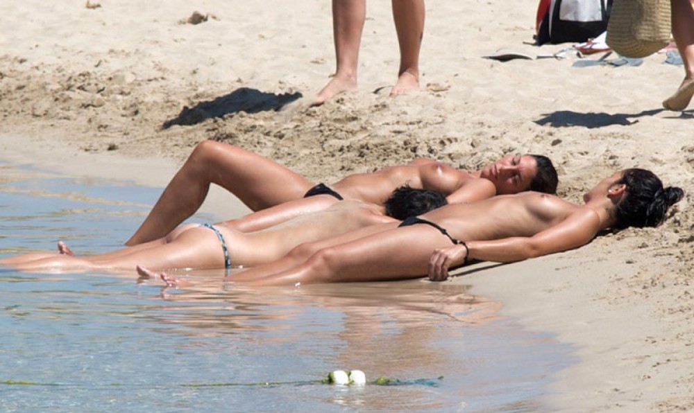 Голые девушки и женины на пляже загорают и купаются. 